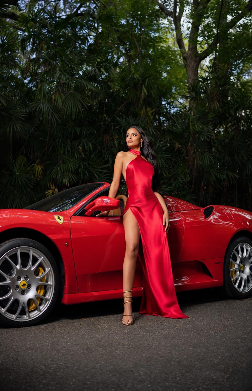 Liz in a red silk gown beside a Ferrari